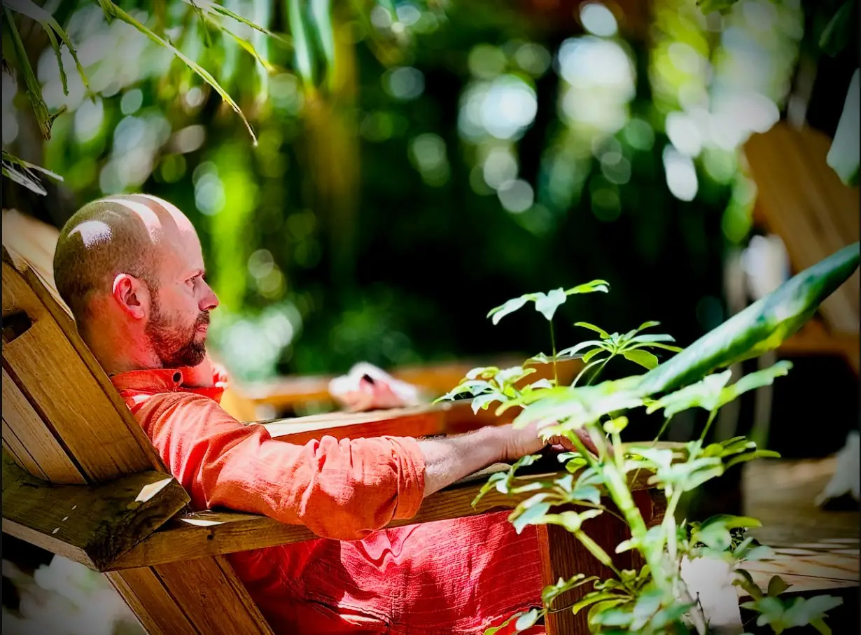 Swami Shambhudevananda resting peacefully in a wooden chair outdoors